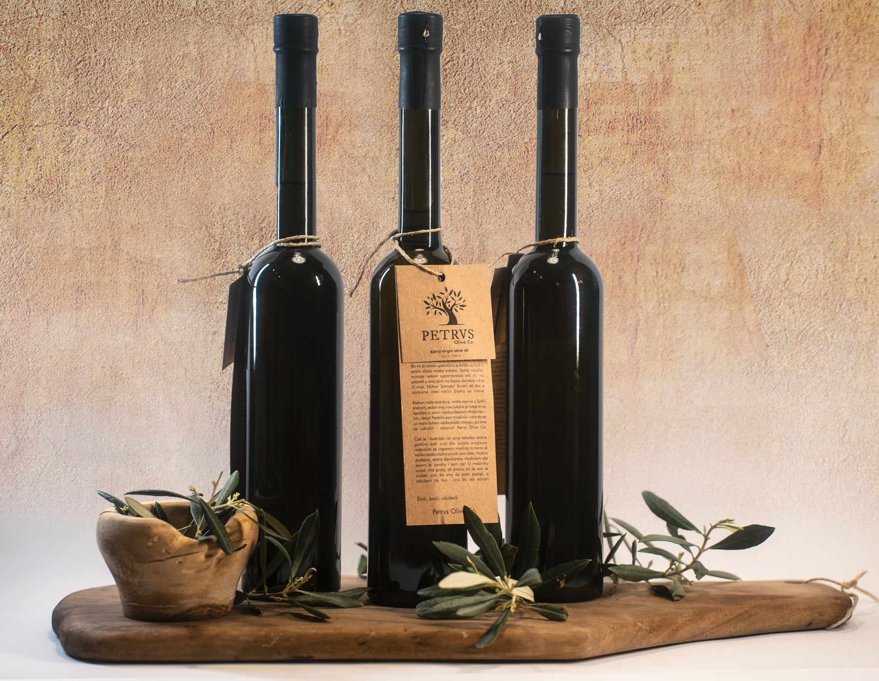 Premium Petrvs olive oil bottles displayed on a wooden board with olive branches against a textured background.